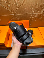 Hermes black slide sandals held in hand, double strap across the top