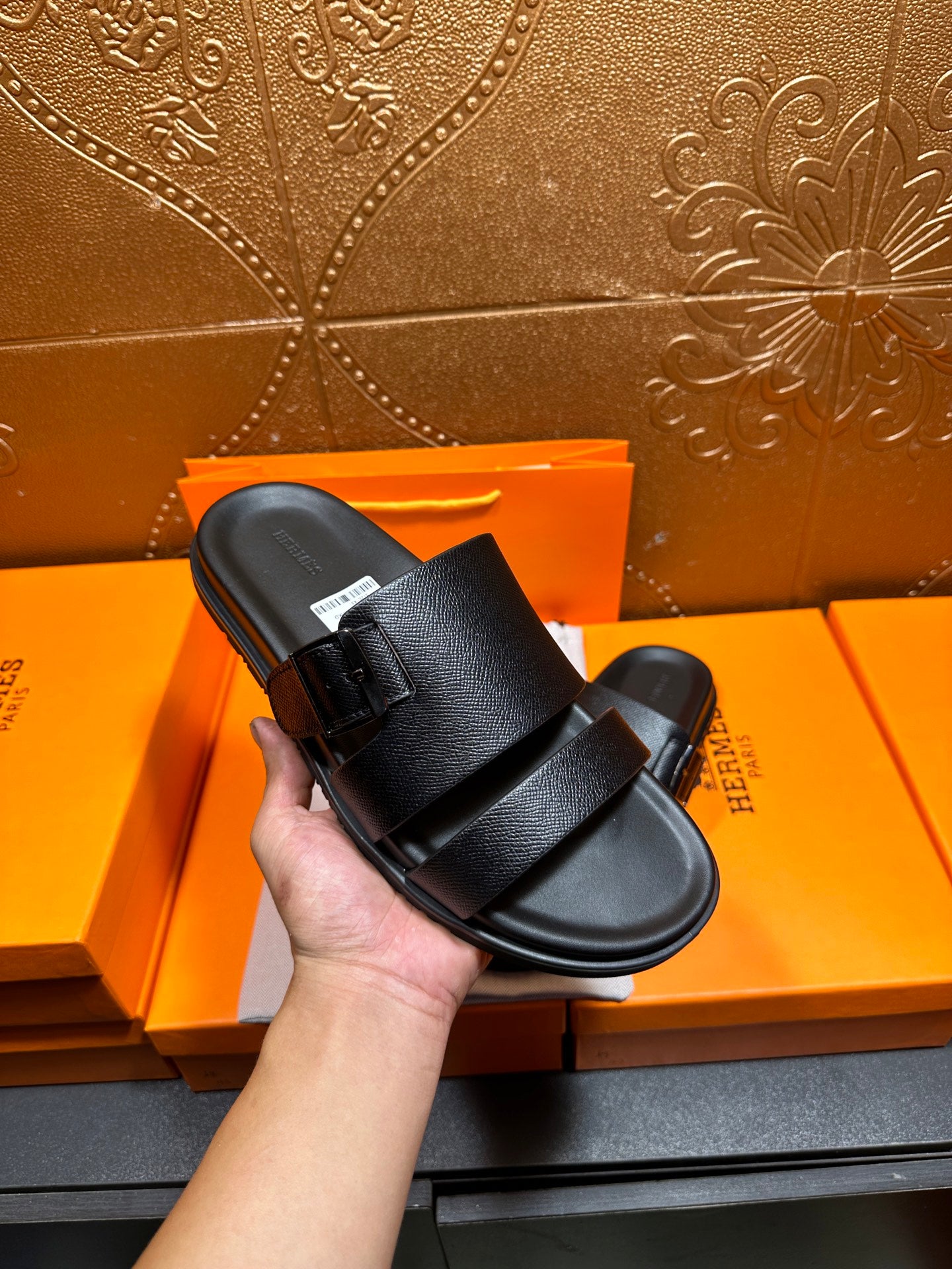 Hermes black slide sandals held in hand, double strap across the top