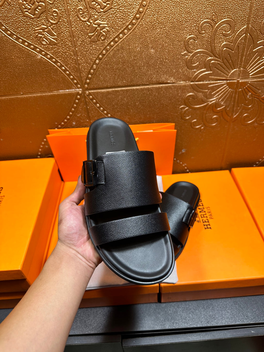 Hermes black leather slide sandals held up, wide strap detail over footbed