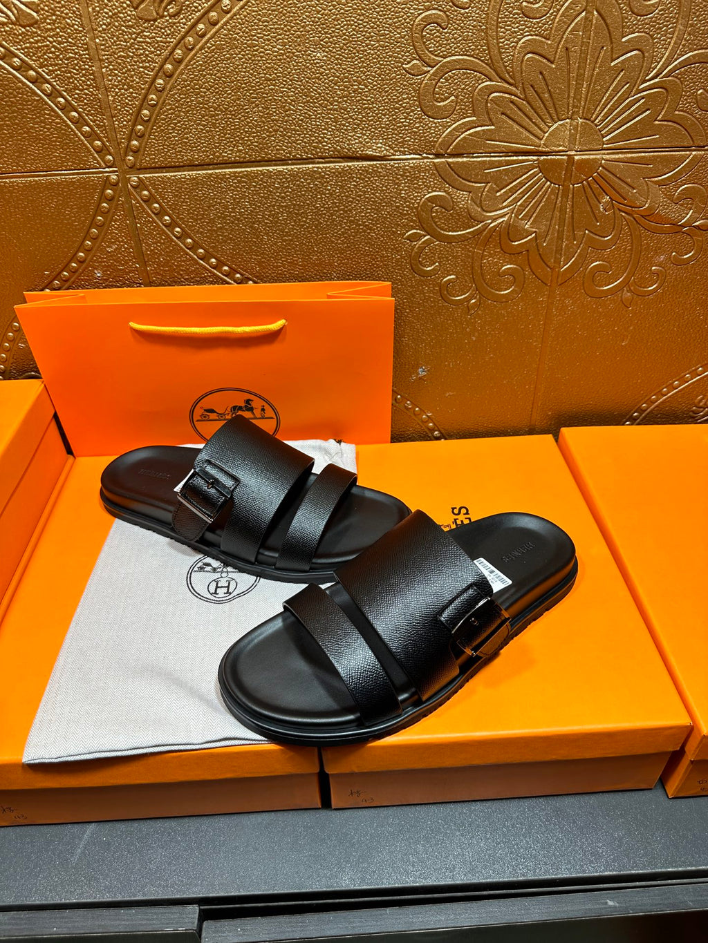Hermes black leather slide sandals with two straps, angled view on shoebox