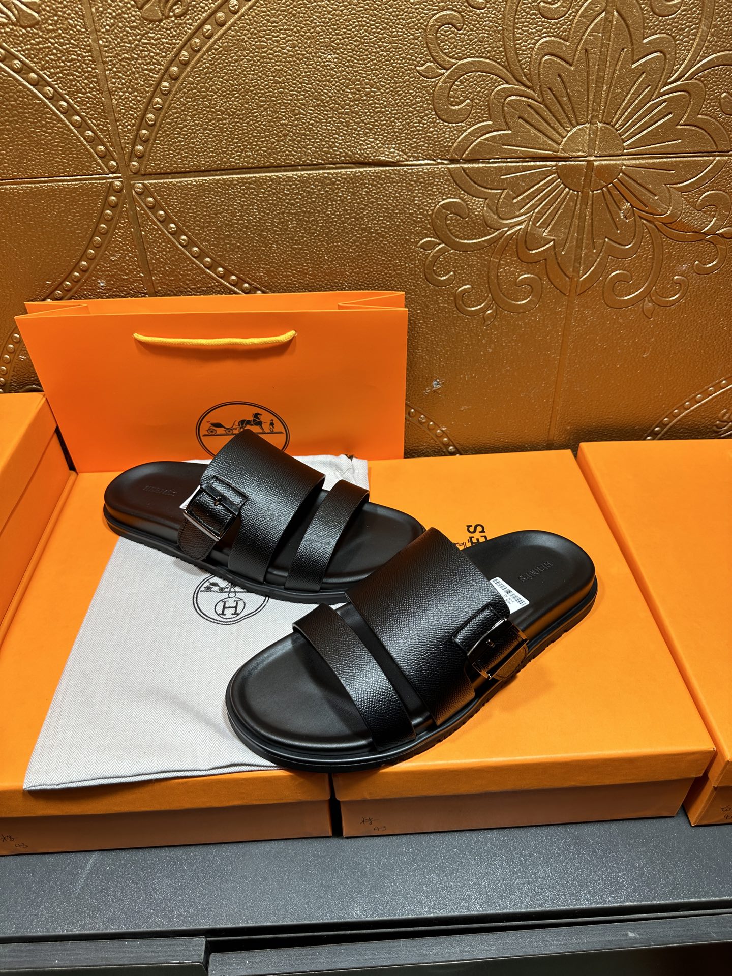 Hermes black leather slide sandals with two straps, angled view on shoebox