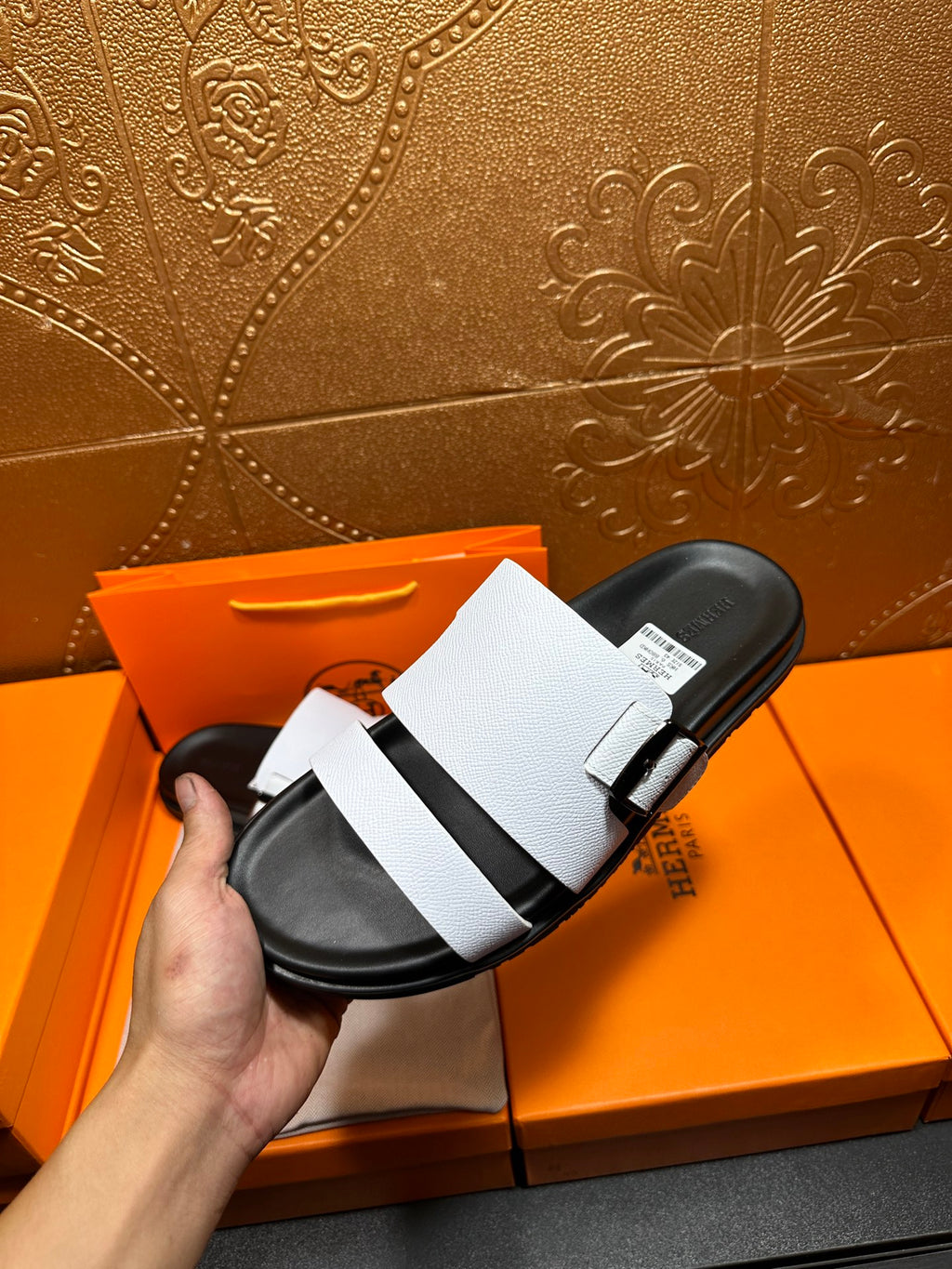 White leather slide sandal with black footbed and strap buckle, held up