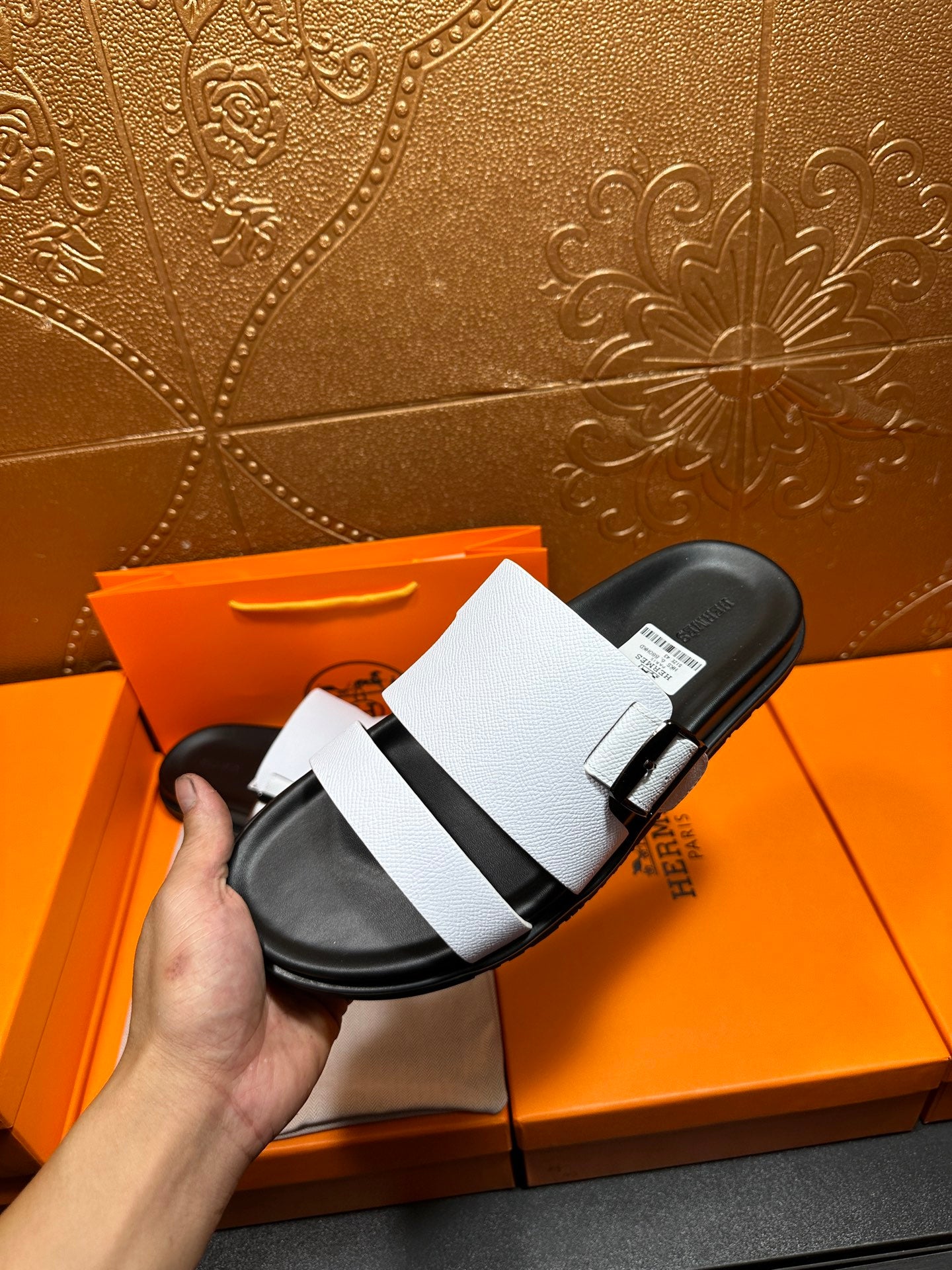 White leather slide sandal with black footbed and strap buckle, held up