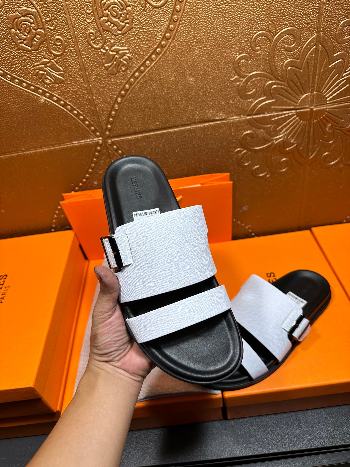 White slide sandals held in hand, showing black footbed and strap