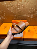 Hermes tan-brown leather sandal held in hand, two wide straps and buckle