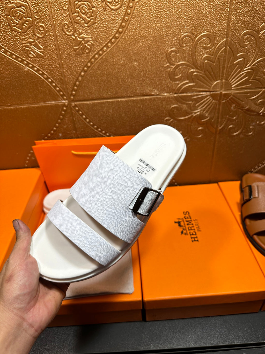 Hermes white leather slide sandals held up, two straps and silver buckle, top view