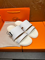 Hermes white leather slide sandals with two wide straps and silver buckle, angled pair