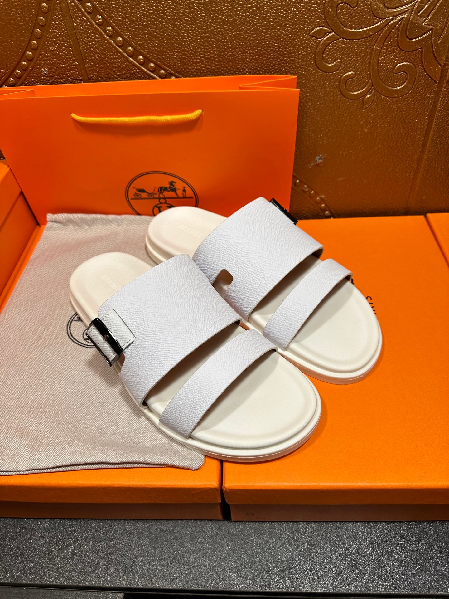 Hermes white leather slide sandals with two wide straps and silver buckle, angled pair