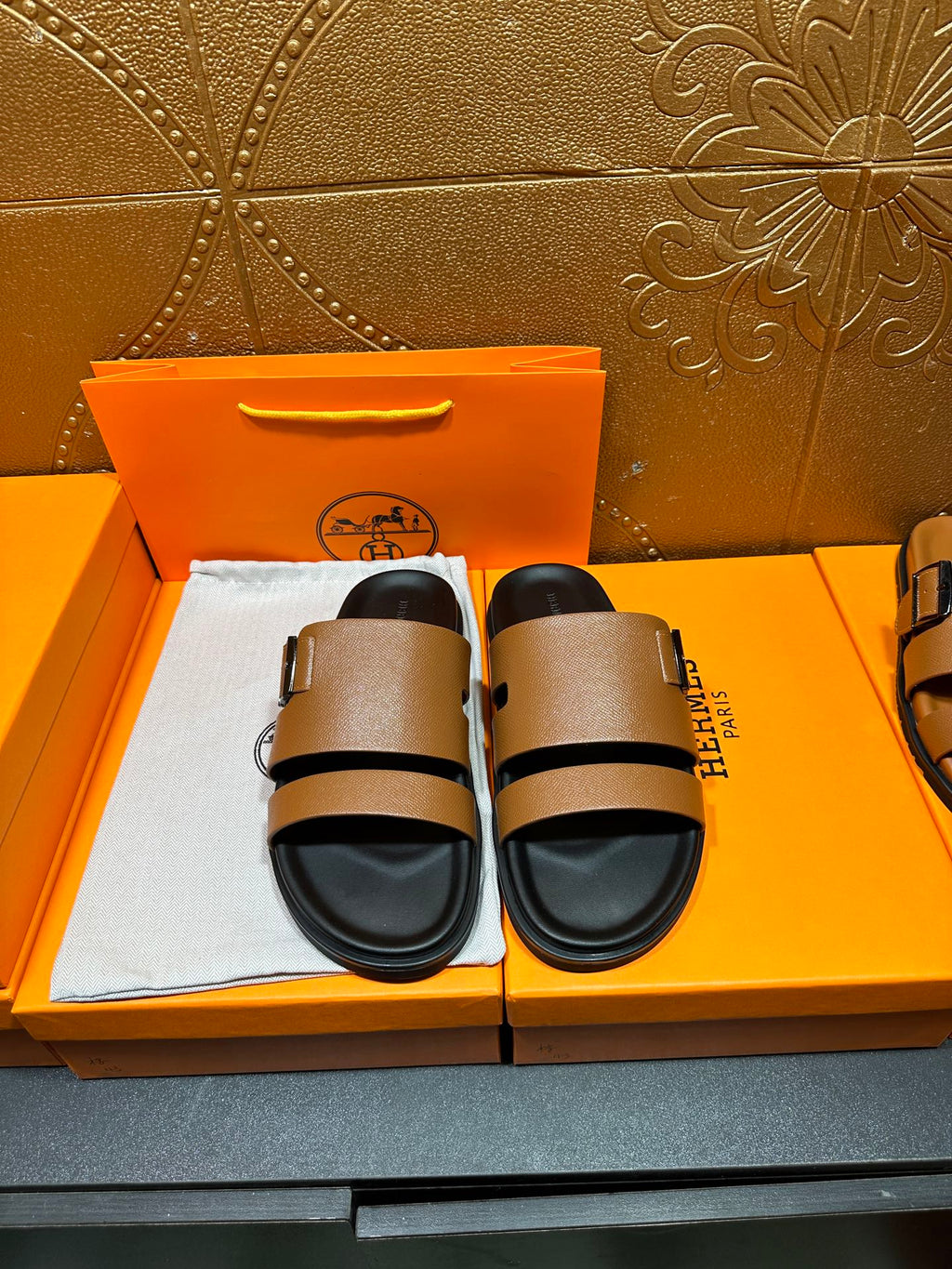 Brown leather slide sandals with black adjustable strap and buckle, black footbed.