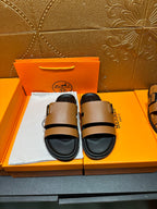 Brown leather slide sandals with black adjustable strap and buckle, black footbed.