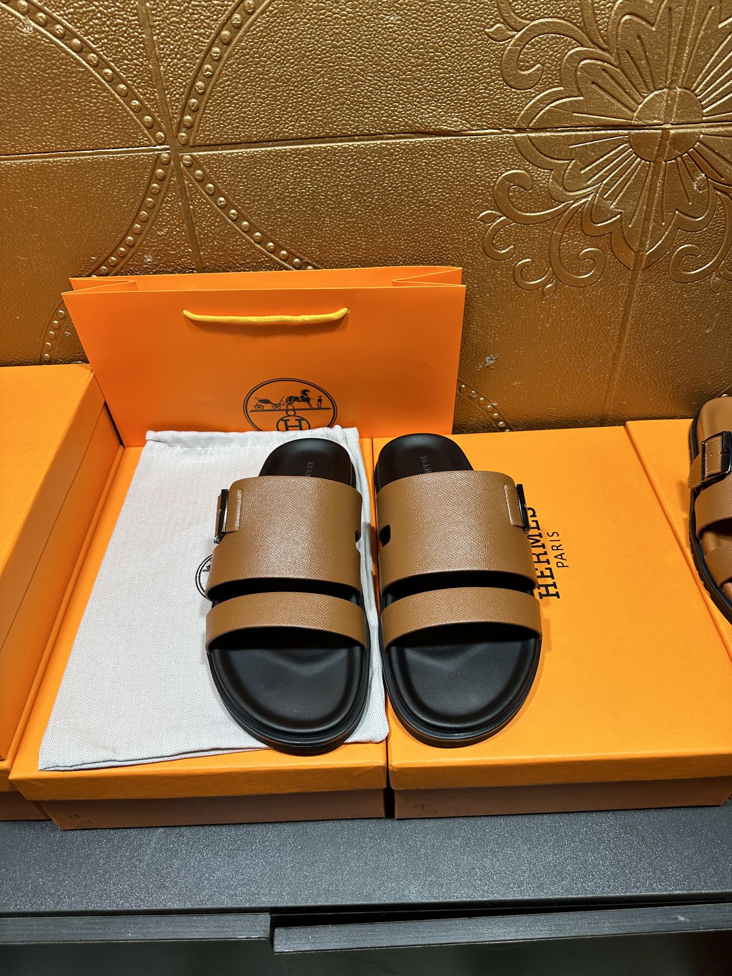 Brown leather slide sandals with black adjustable strap and buckle, black footbed.