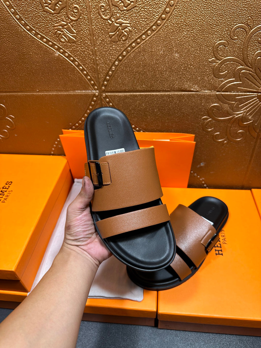 Brown slide sandal with black strap and silver-tone buckle held in hand.