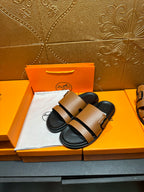Pair of brown slide sandals with black straps and metal buckle over black footbeds.