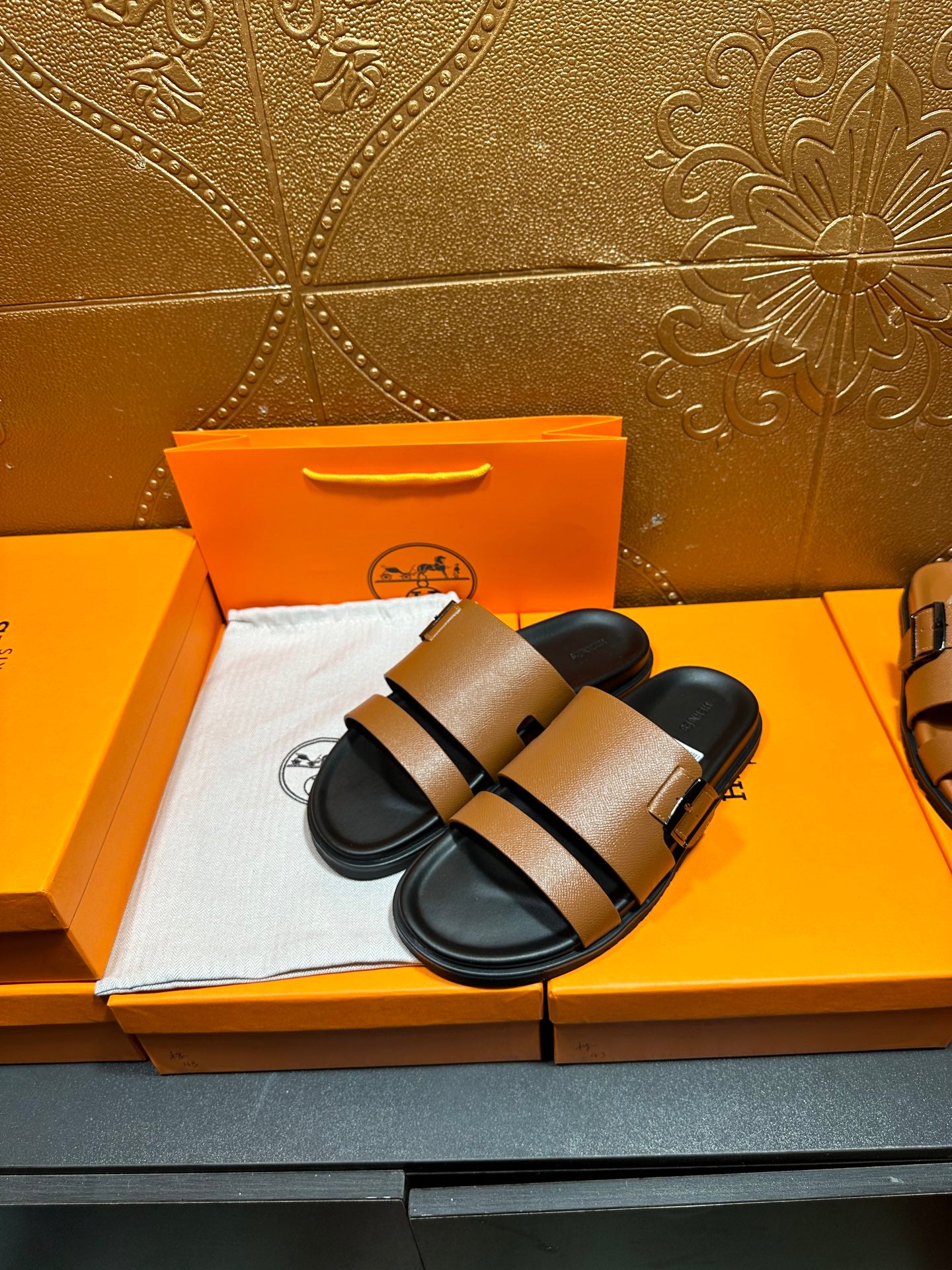Pair of brown slide sandals with black straps and metal buckle over black footbeds.