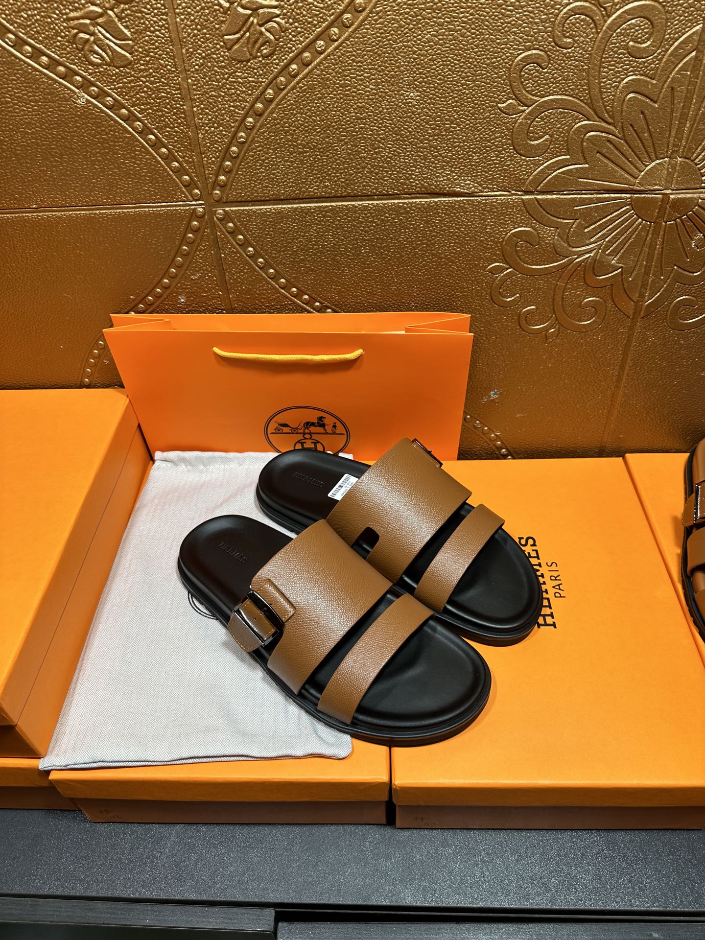 Tan-brown slide sandals with black strap and metal buckle, black sole.