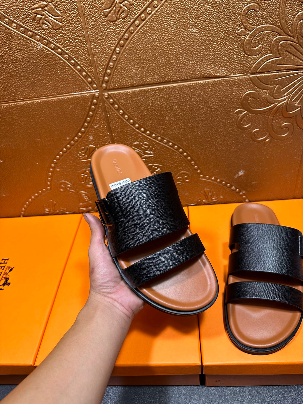 Black slide sandal with two wide straps, held by hand, tan footbed