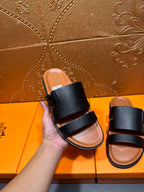 Black slide sandal with two wide straps, held by hand, tan footbed