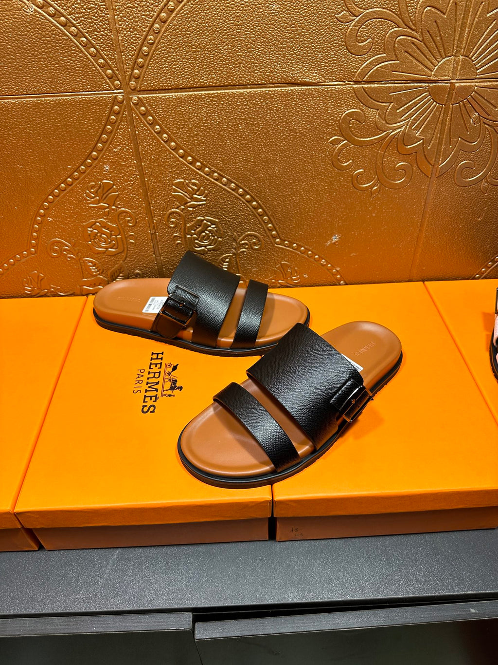 Black slide sandals with two wide straps and tan footbeds, paired side view