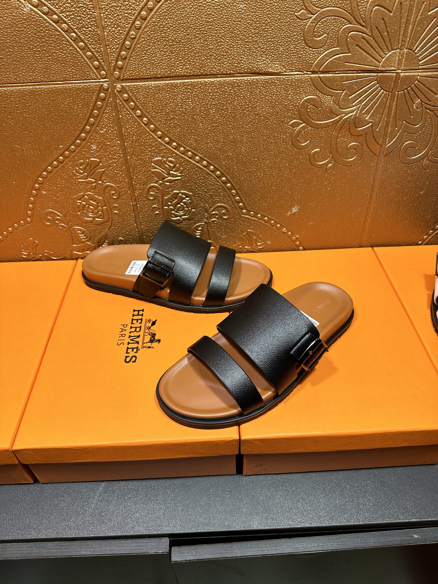 Black slide sandals with two wide straps and tan footbeds, paired side view