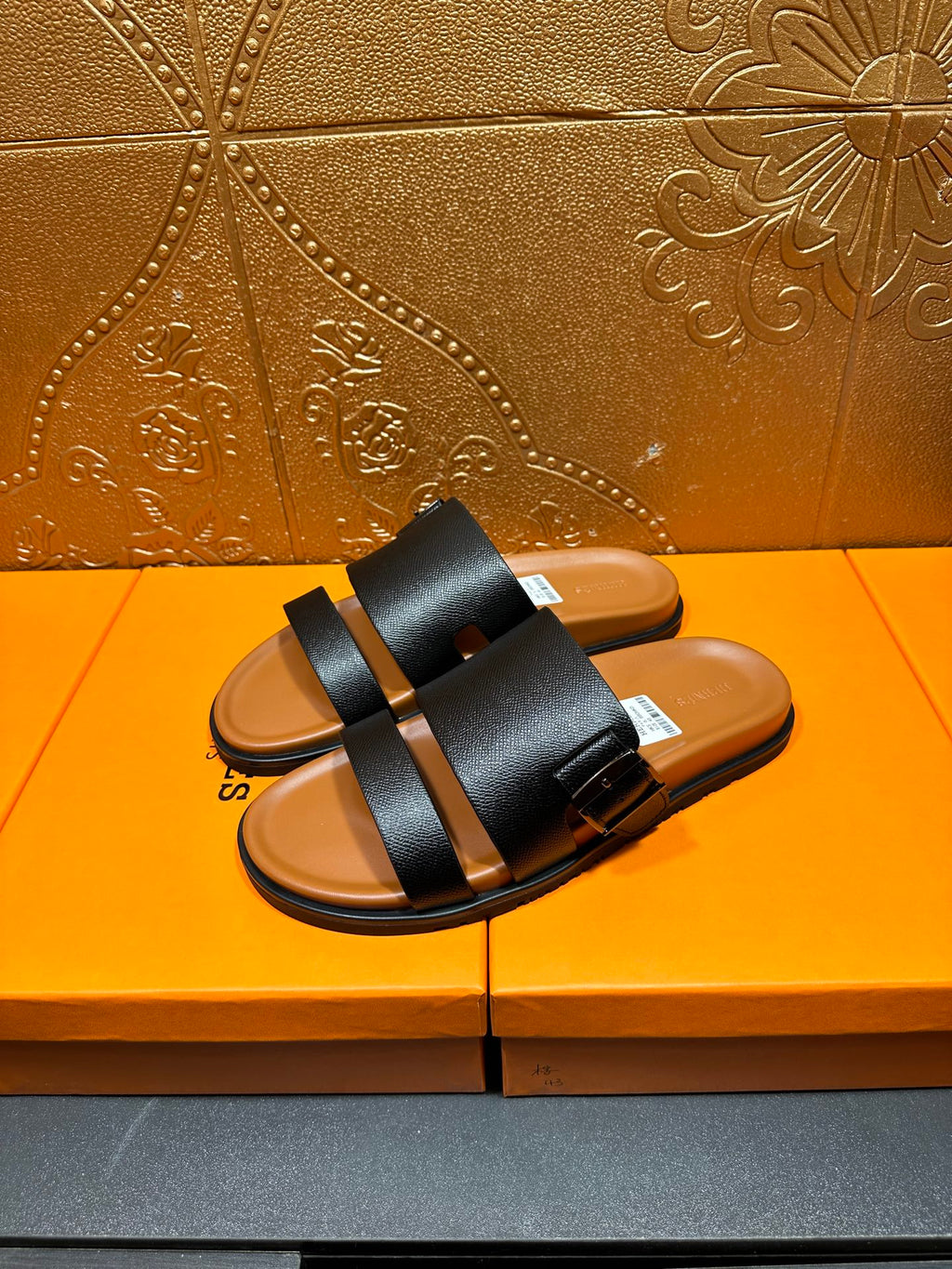 Black slide sandals with two wide straps and tan footbeds, pair standing view