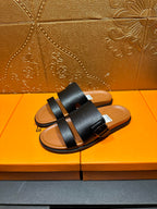 Black slide sandals with two wide straps and tan footbeds, pair standing view