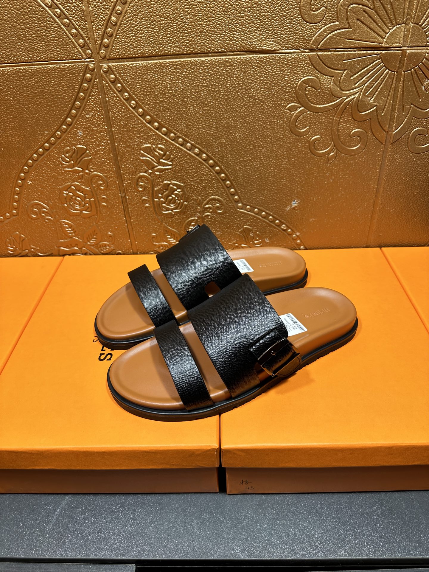 Black slide sandals with two wide straps and tan footbeds, pair standing view