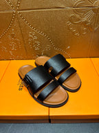 Black slide sandals with two wide straps over tan footbeds, angled top view