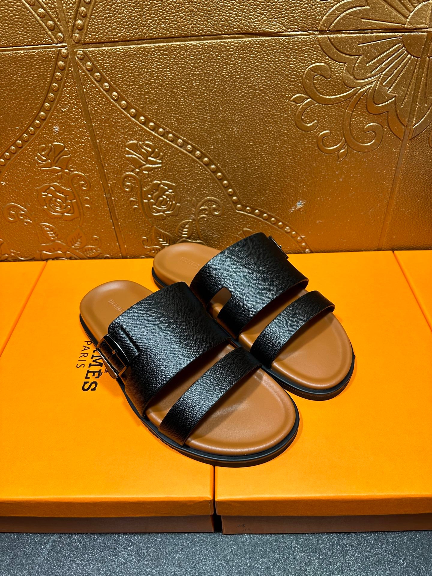 Black slide sandals with two wide straps over tan footbeds, angled top view