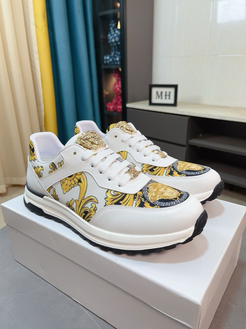 White leather-style sneakers with gold ornate print, lace-up front, and chunky sole
