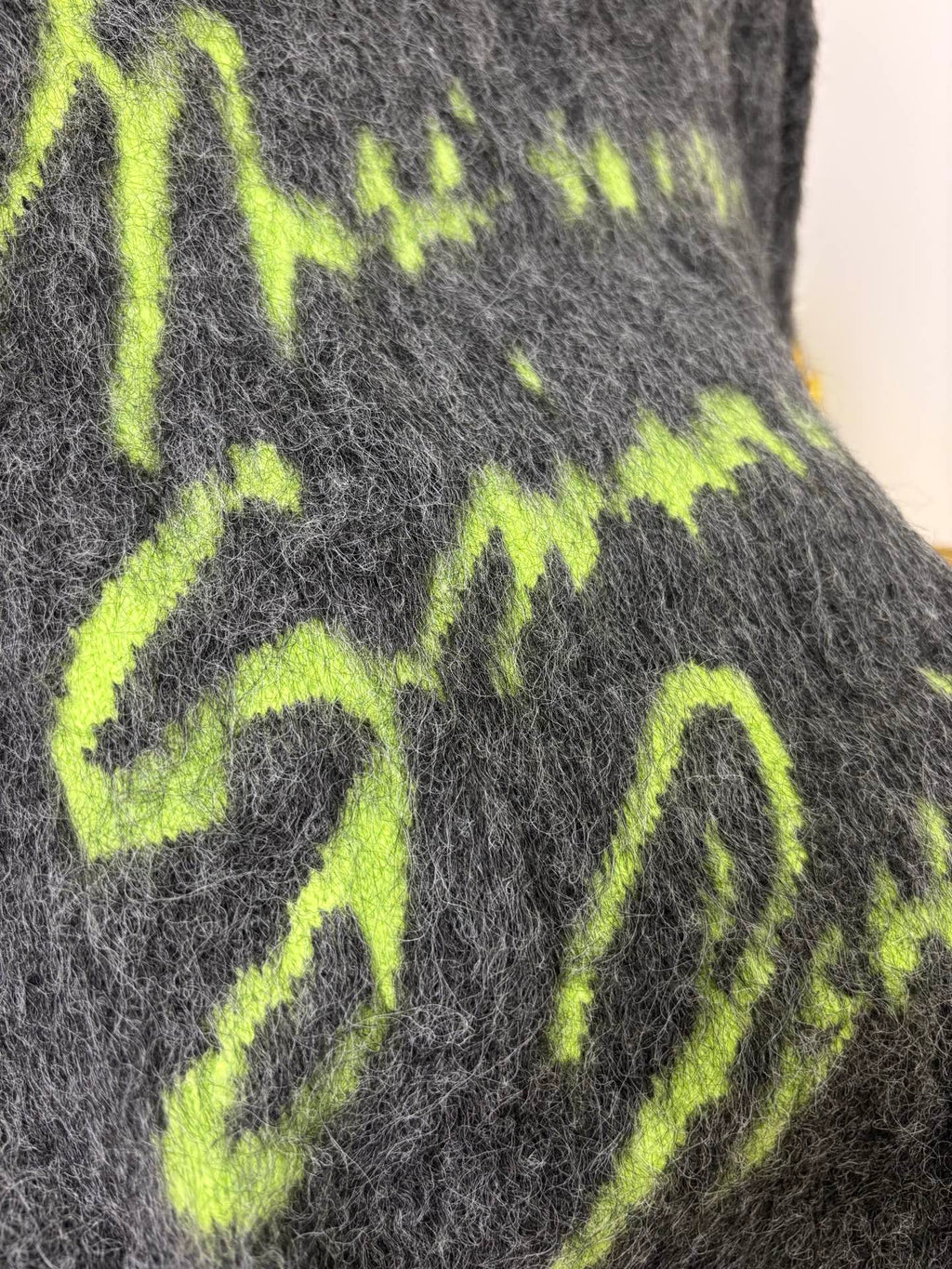 Neon green graphic lettering on dark gray fuzzy sweater fabric, close-up