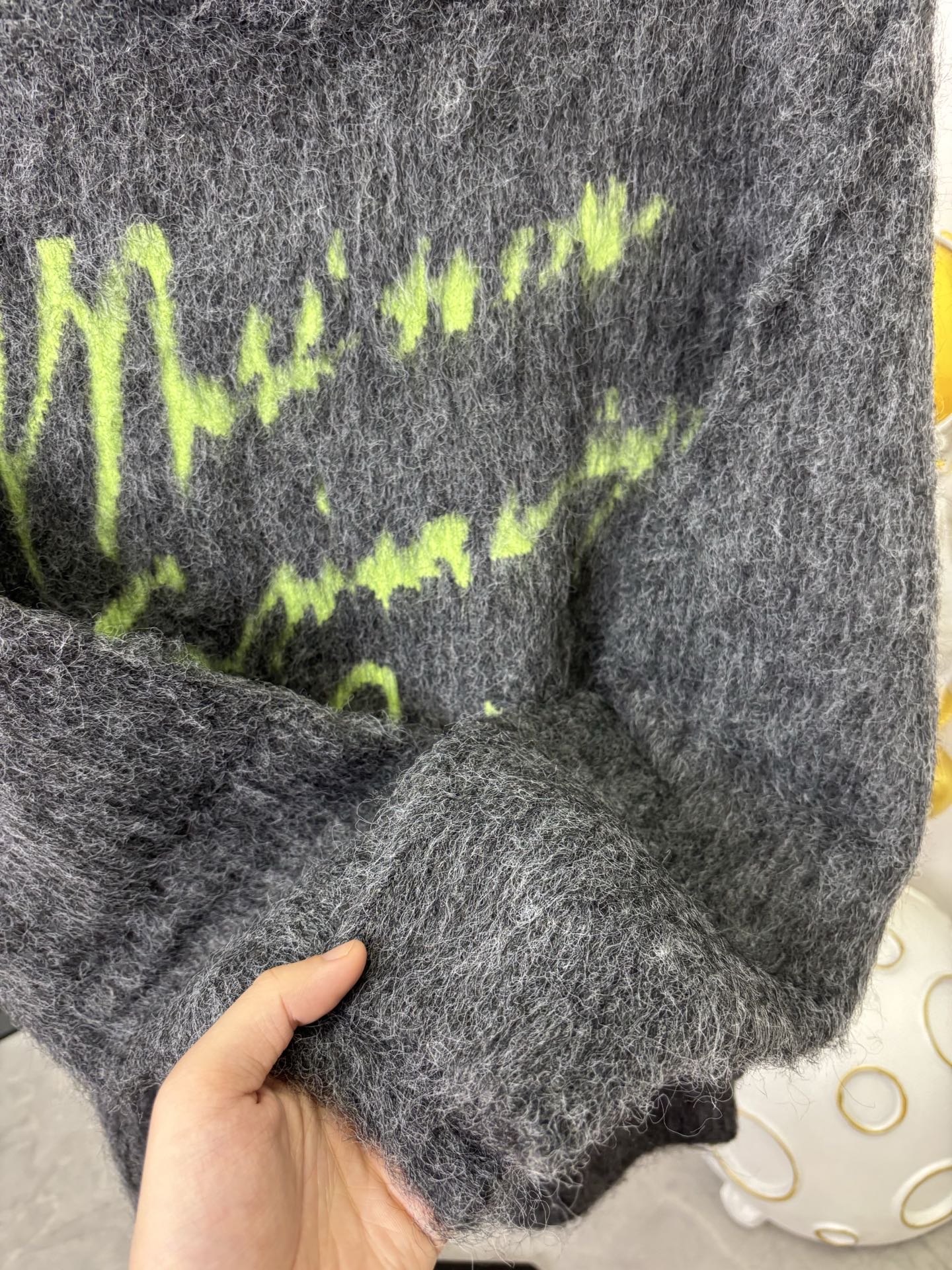 Dark gray fuzzy sweater hem with hand holding fabric, close-up