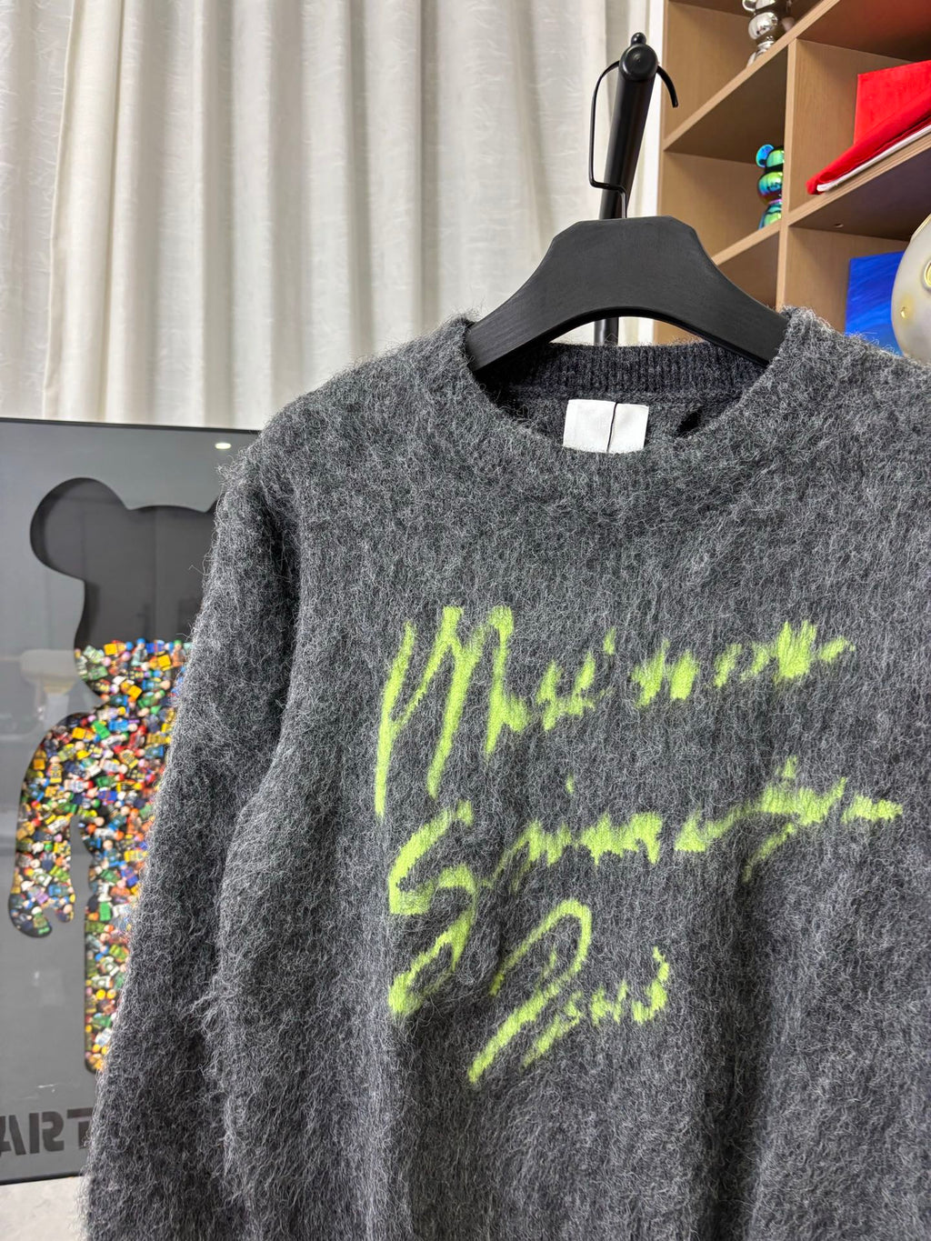 Dark gray fuzzy crewneck sweater with neon green graphic print, close-up