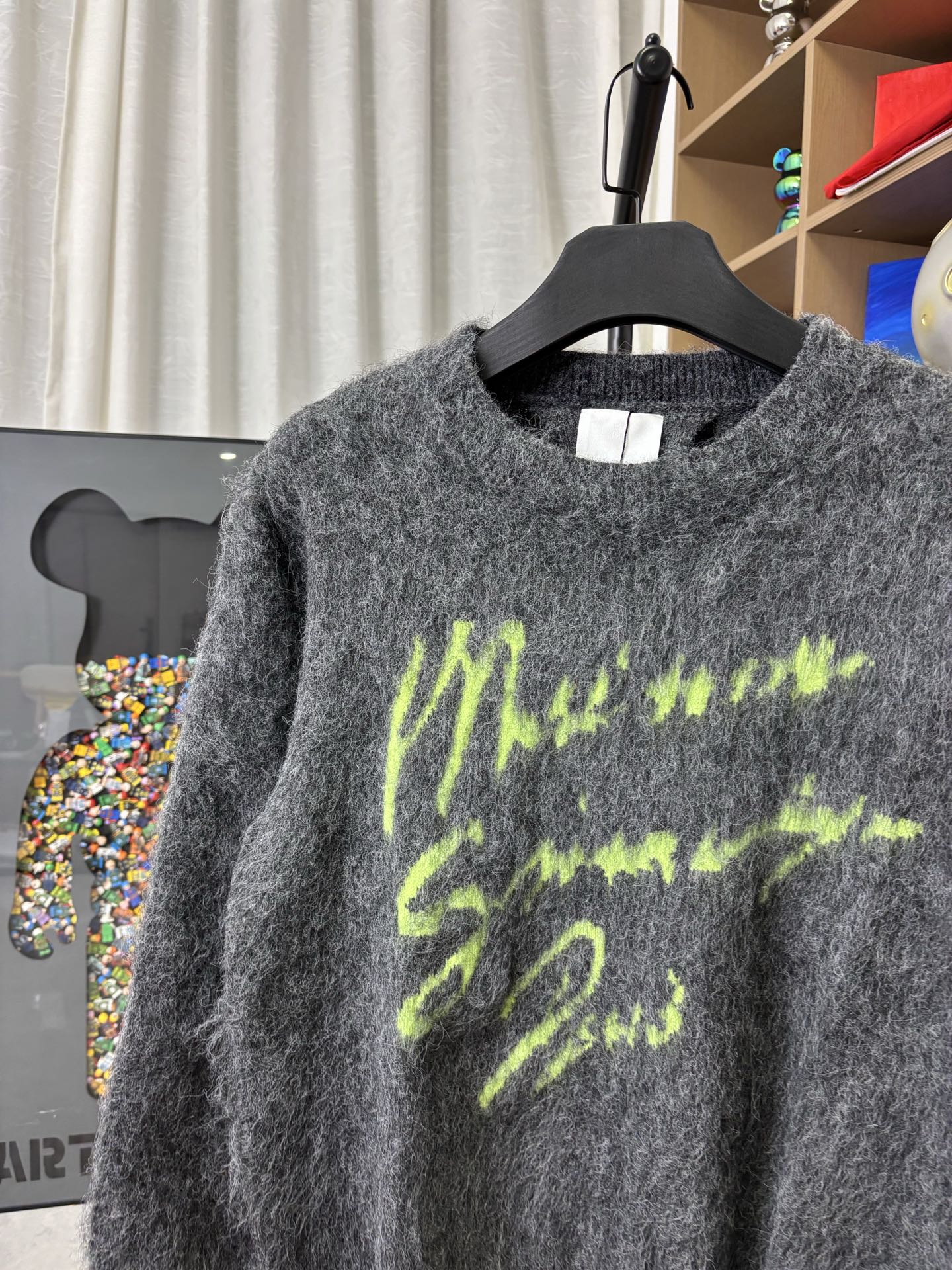 Dark gray fuzzy crewneck sweater with neon green graphic print, close-up