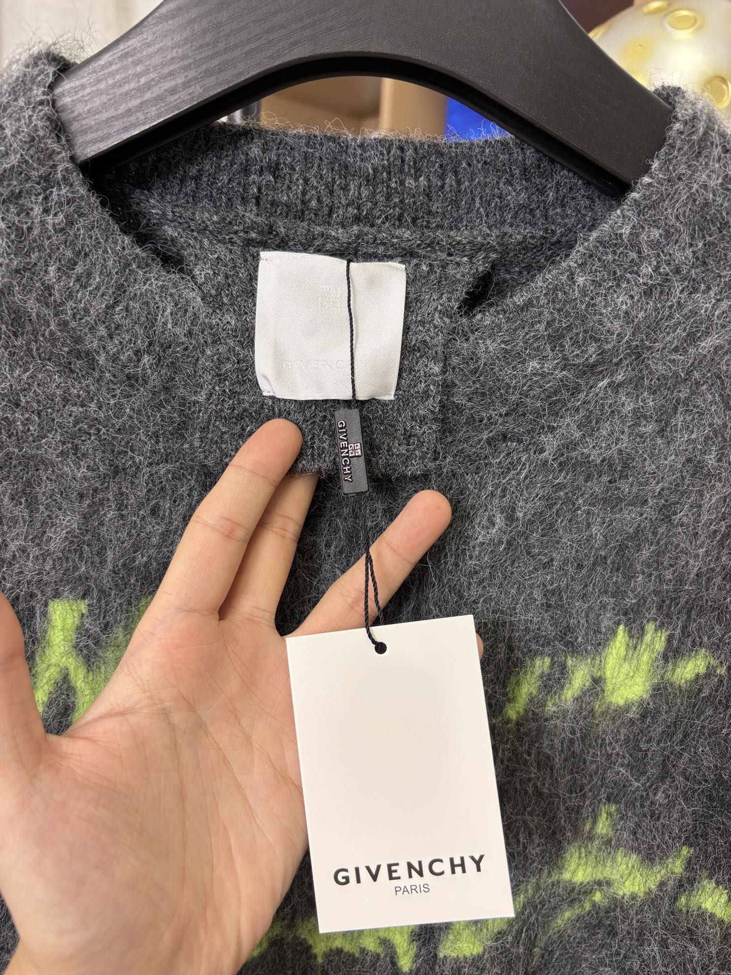 Dark gray sweater neckline with white label and GIVENCHY tag, close-up