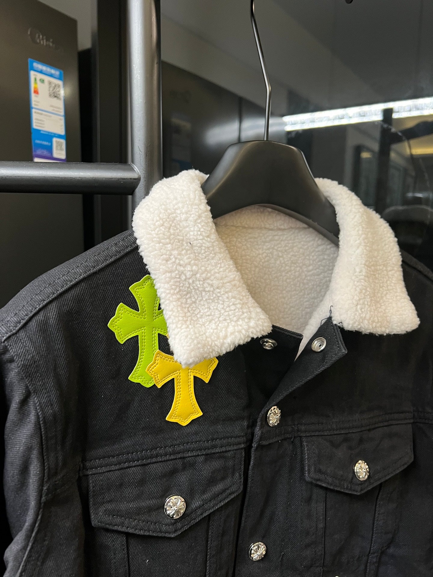 Black denim jacket with sherpa collar, lime/yellow cross patch on chest, button front