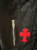 Black denim jacket pocket close-up with gold zipper and red cross patch applique