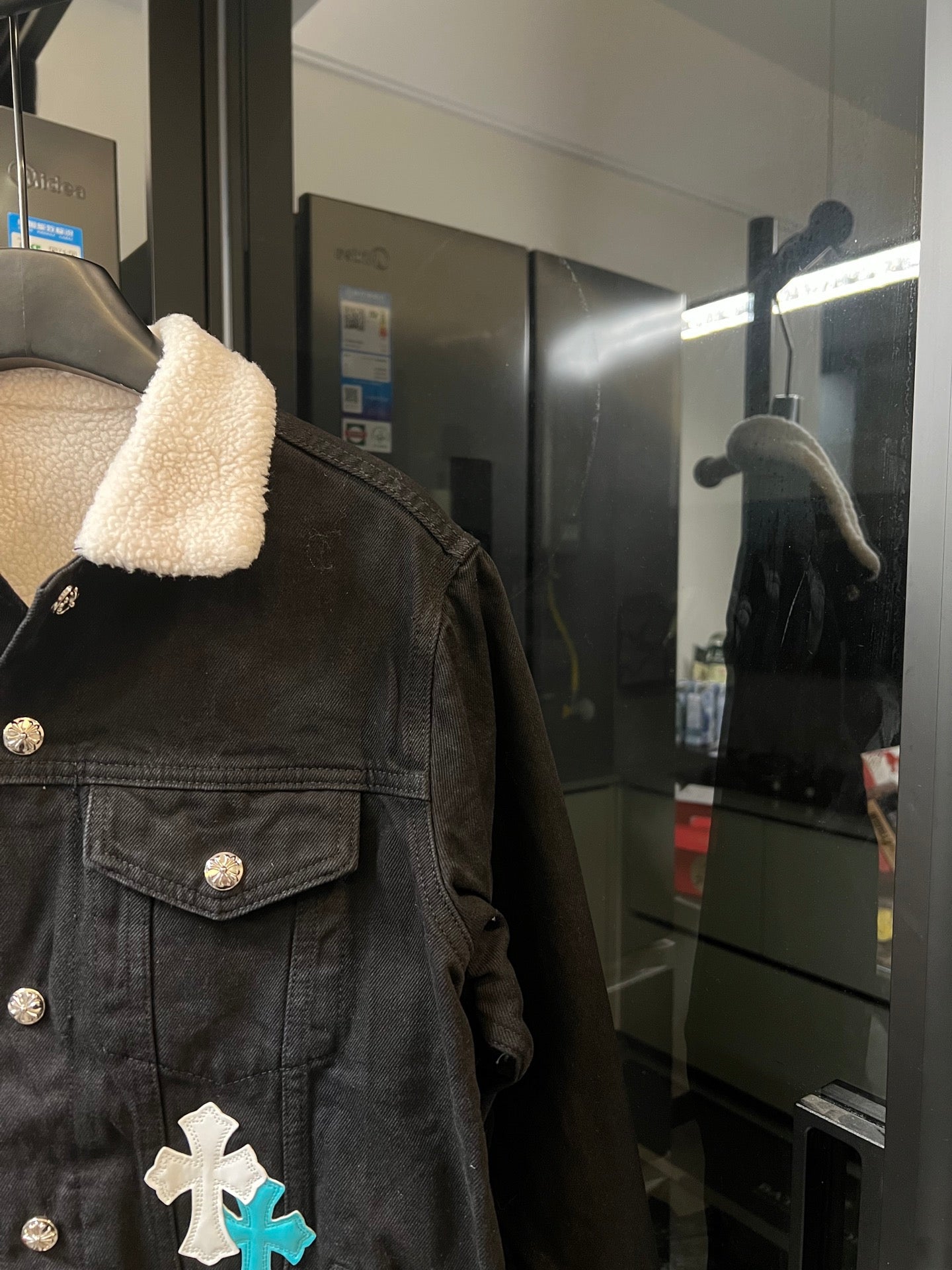 Black denim jacket with sherpa collar, gold zip pocket and white/blue cross patch