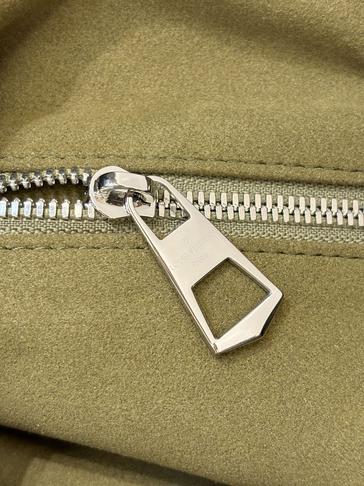 Silver-tone zipper pull on olive green leather bag with engraved bar