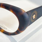 Tortoiseshell eyeglass temple with gold medallion logo and Greek key pattern