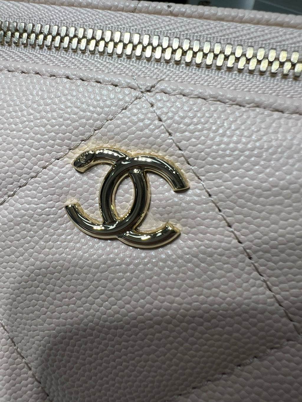 Chanel bag hardware close-up with CC emblem on textured light leather.