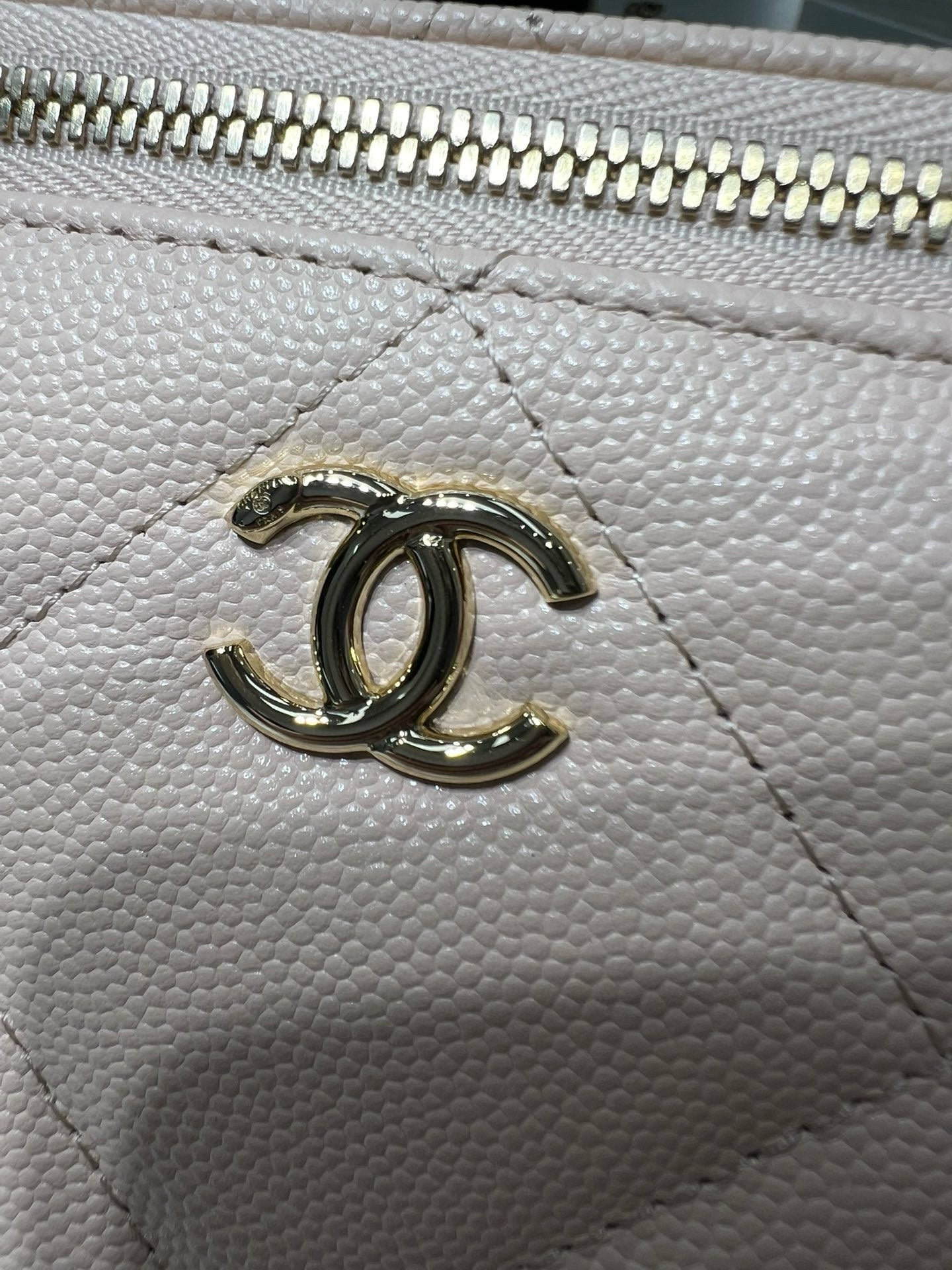 Chanel bag hardware close-up with CC emblem on textured light leather.