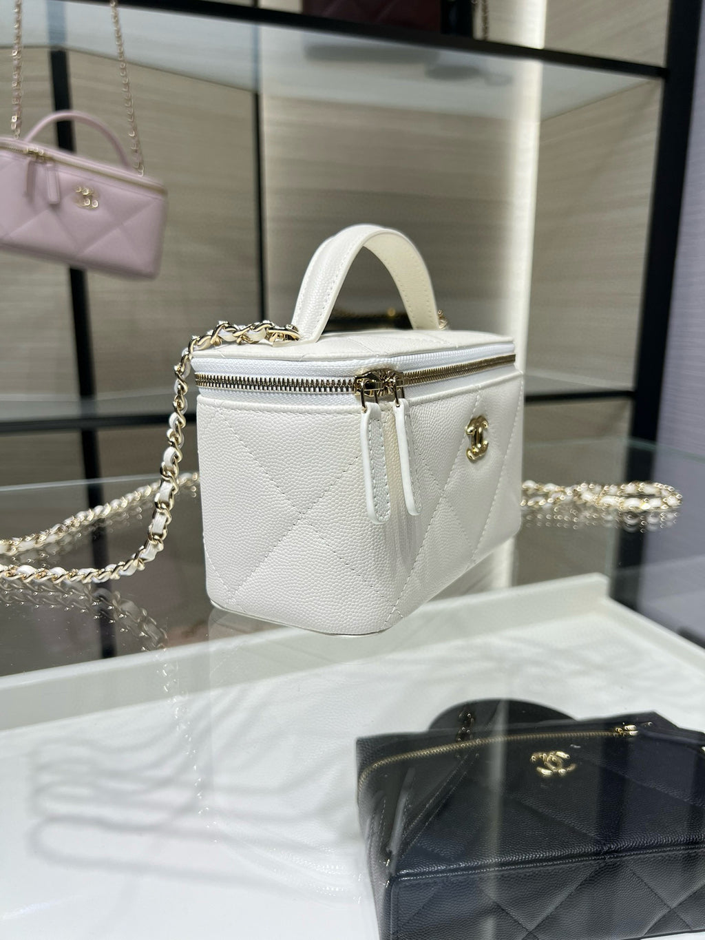 White structured mini handbag with top handle, gold chain strap, and zipper front.