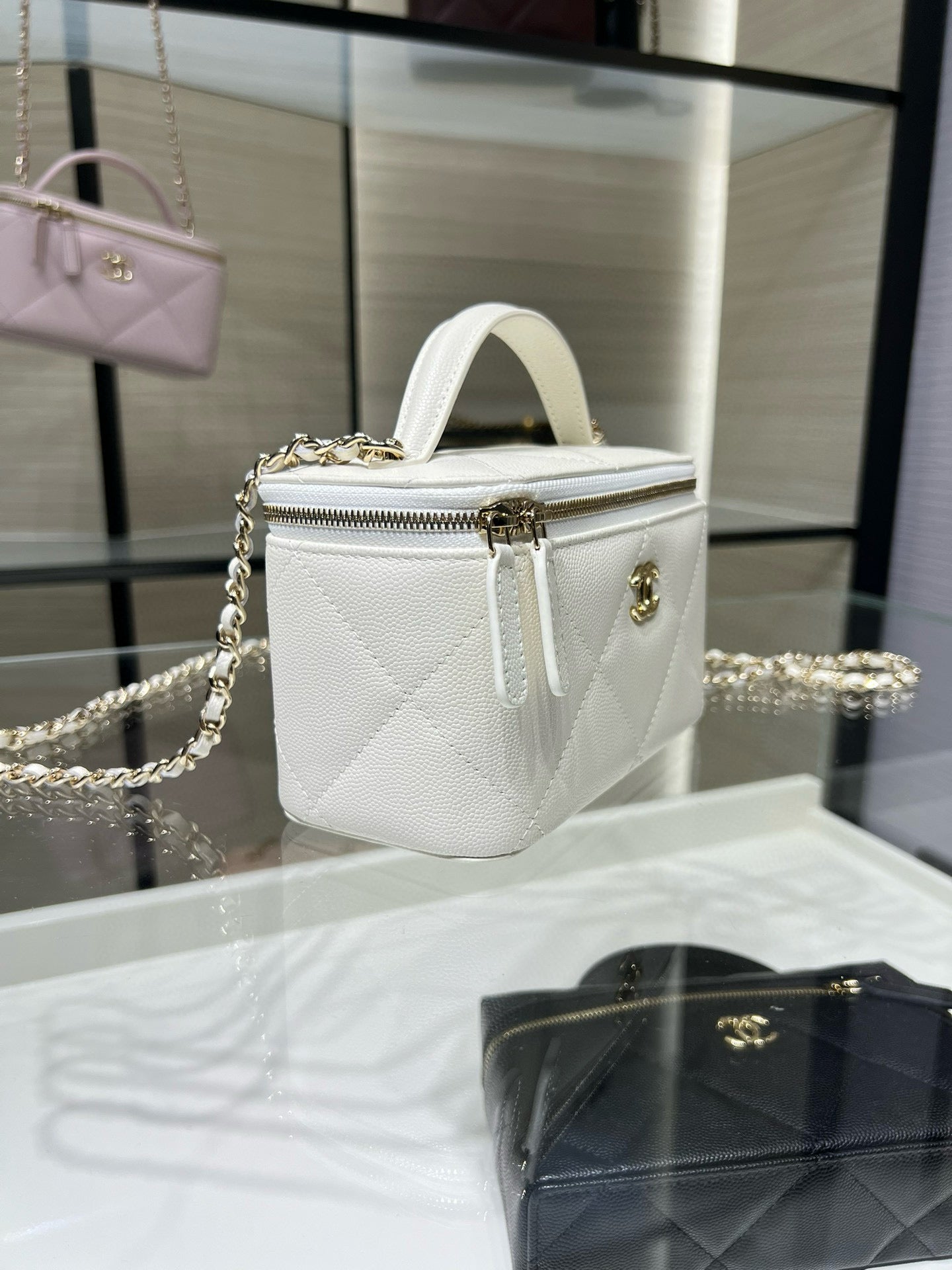 White structured mini handbag with top handle, gold chain strap, and zipper front.