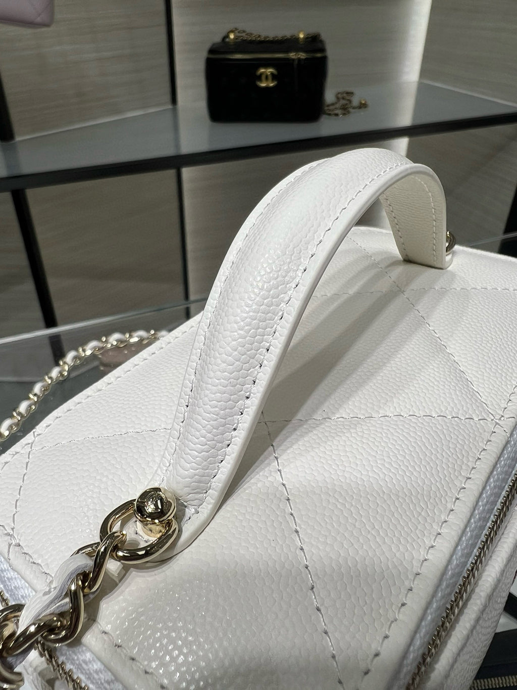 Close-up of white leather handbag top handle with gold chain strap connector.