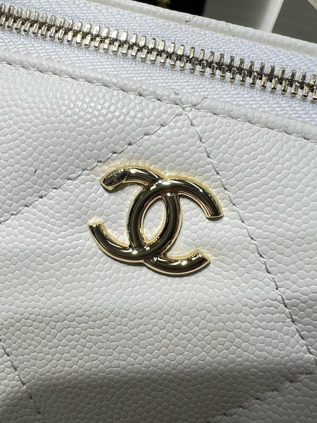 Close-up of white quilted handbag with gold CC logo on the front panel.
