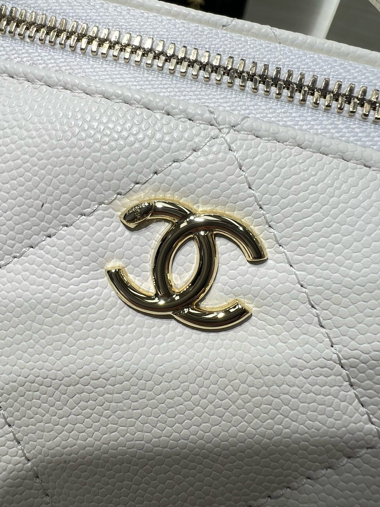 Close-up of white quilted handbag with gold CC logo on the front panel.
