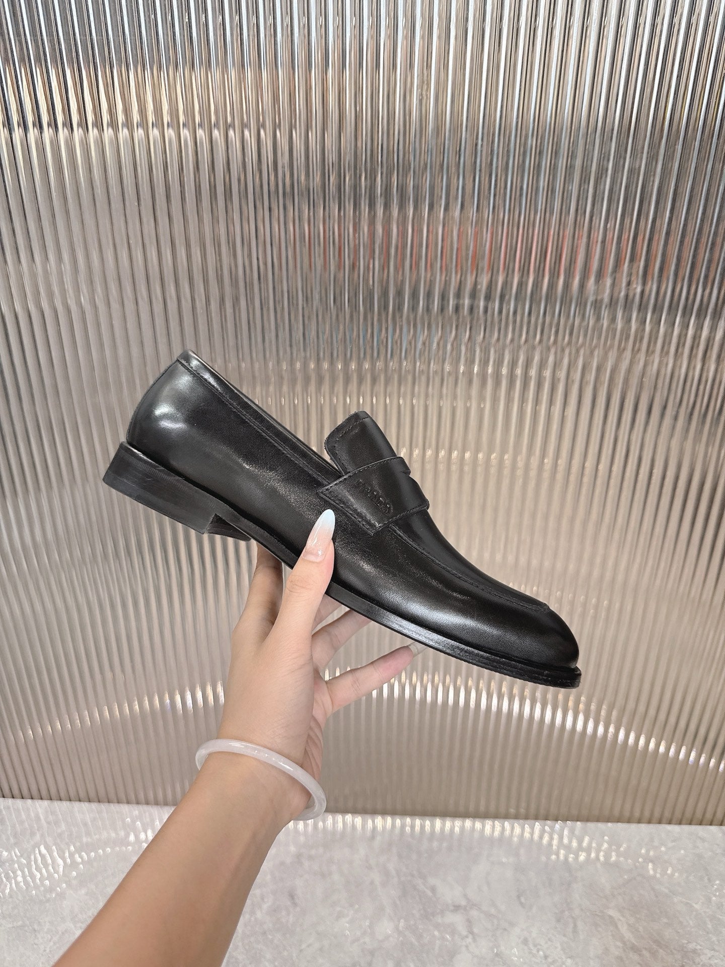 Black leather loafer with strap detail, side view, held in hand