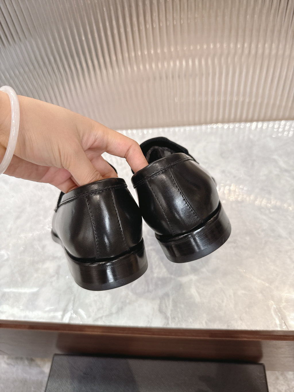 Black leather loafers held side-by-side by hand, showing slip-on back