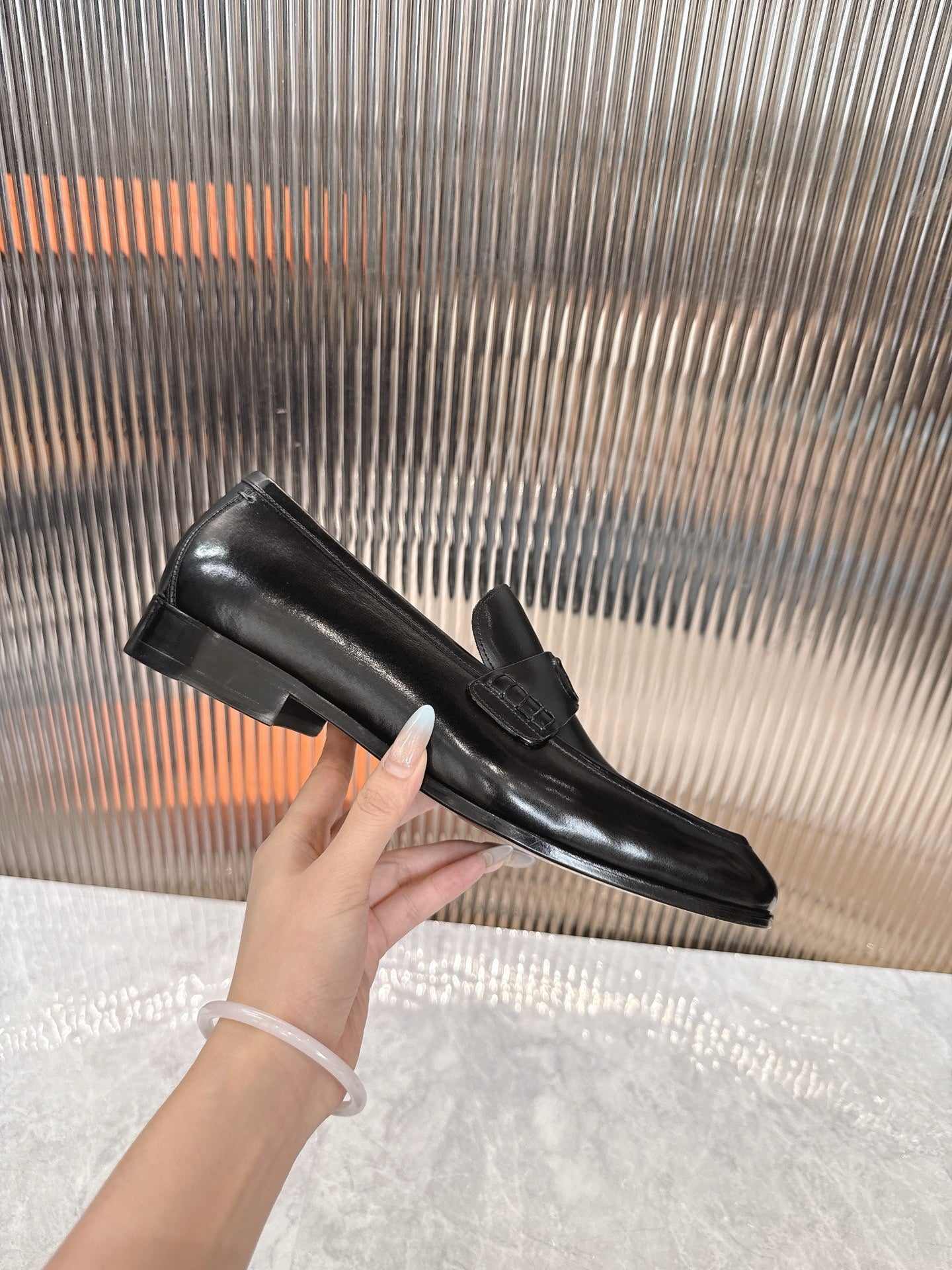 Black leather unisex loafer held in hand, flat outsole visible.