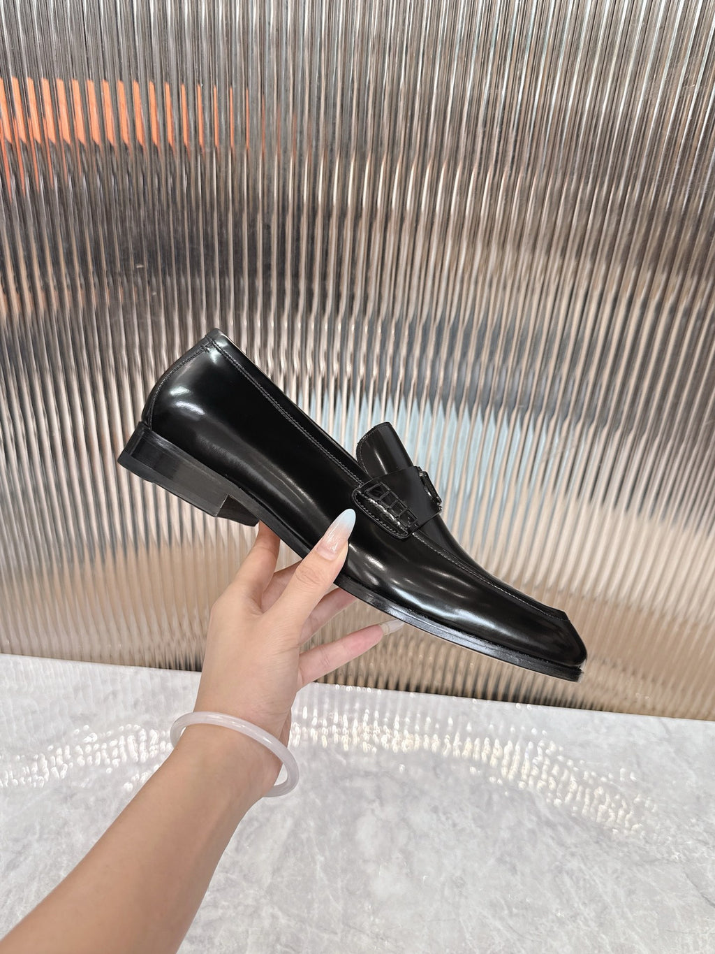 Single Dior black leather loafer held in hand, glossy finish and buckle